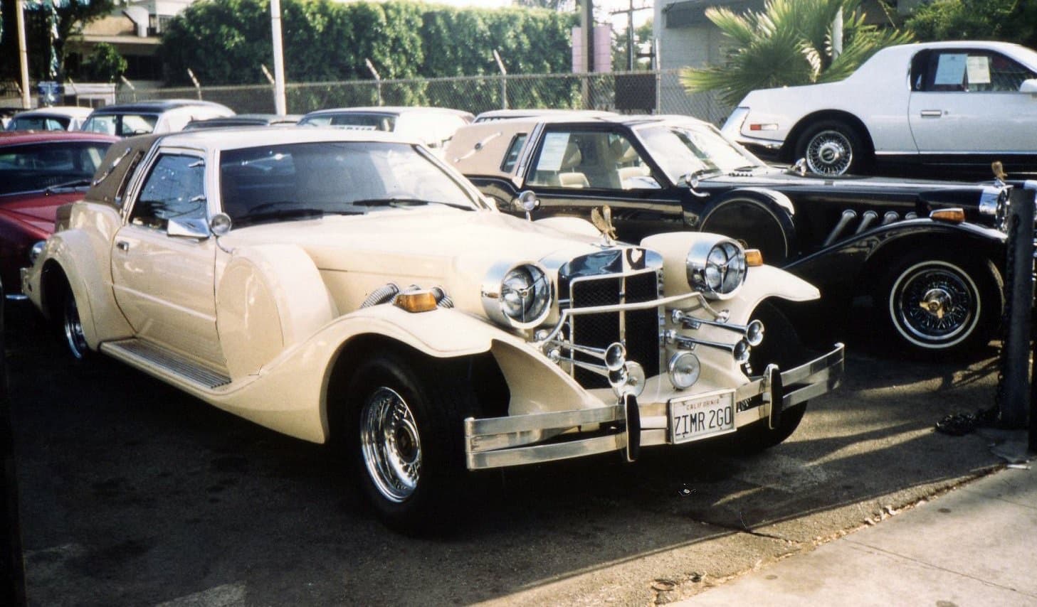 A cream and a black Golden Spirit coupé side by side on a Los Angeles used-car lot in a faded colour photograph.