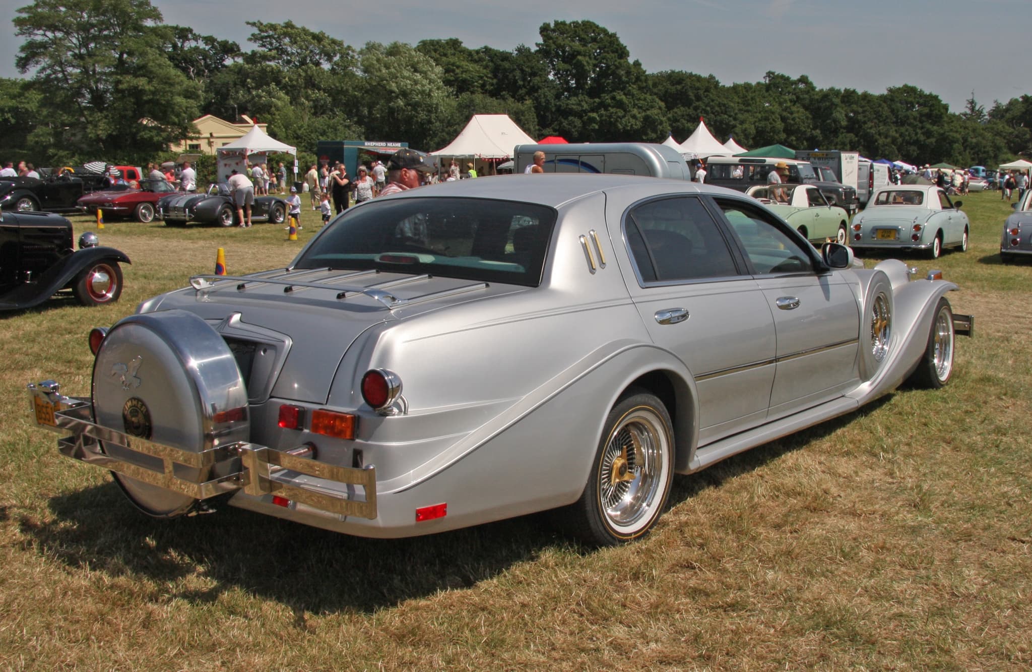 The rear of a silver four-door Golden Spirit with a continental spare wheel and a luggage rack on a show field.