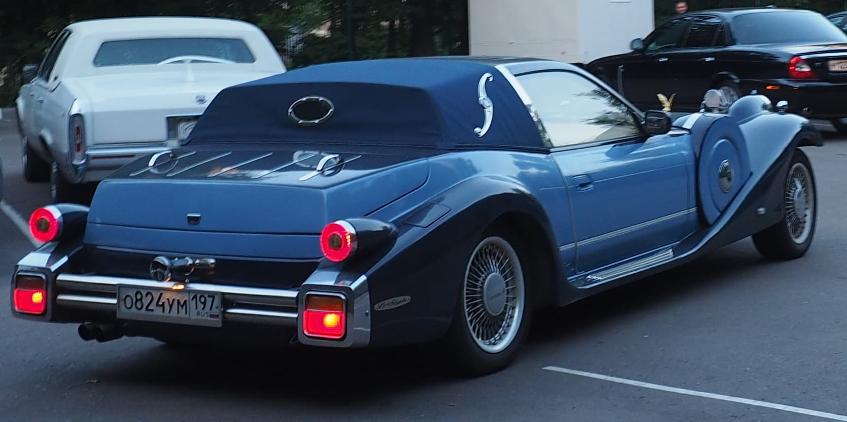 A two-tone blue Mitsuoka Le-Seyde with a padded rear roof and round tail lamps, seen from behind in a car park.
