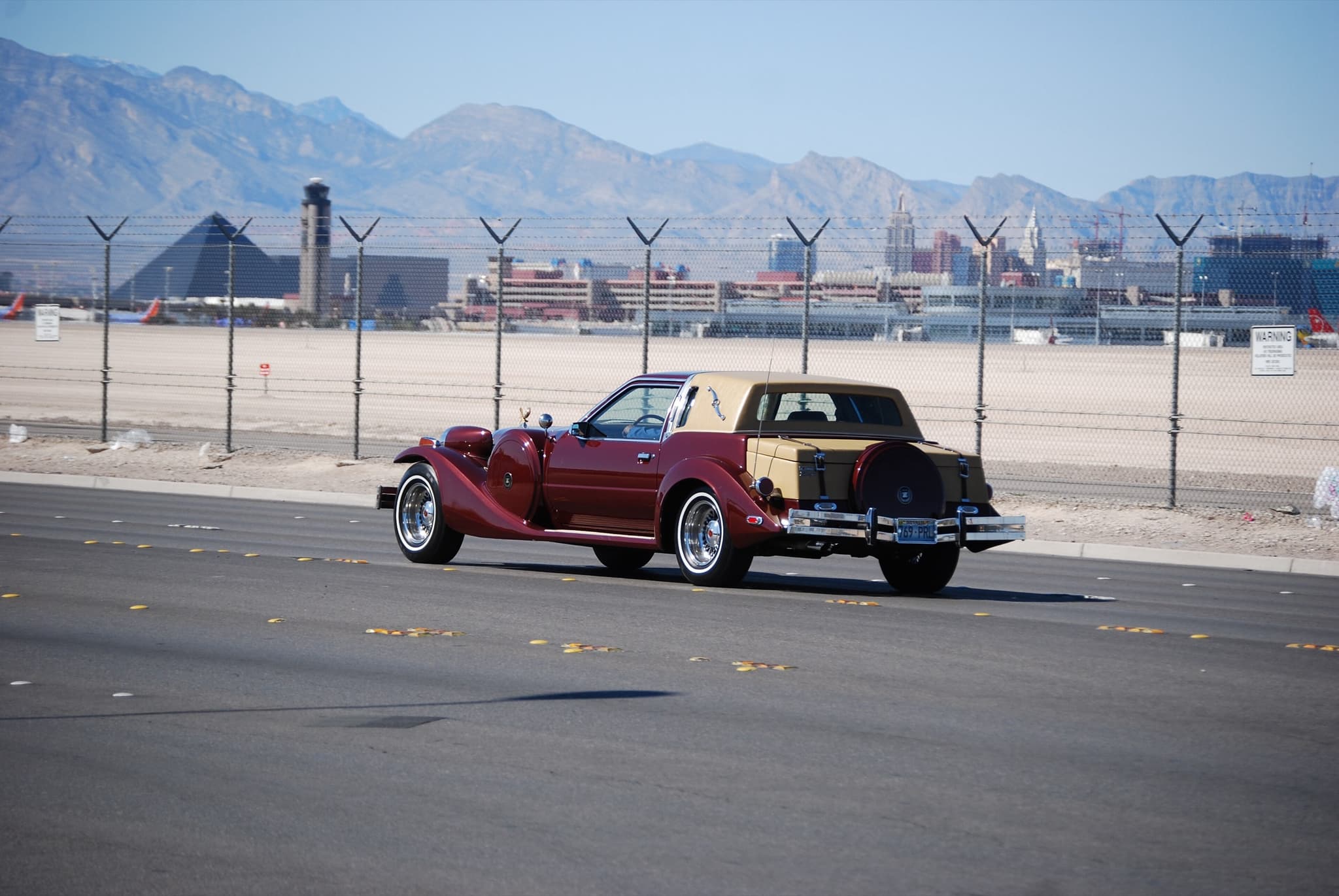 A maroon and tan Golden Spirit coupé driving along a desert road with the Las Vegas skyline and mountains behind.