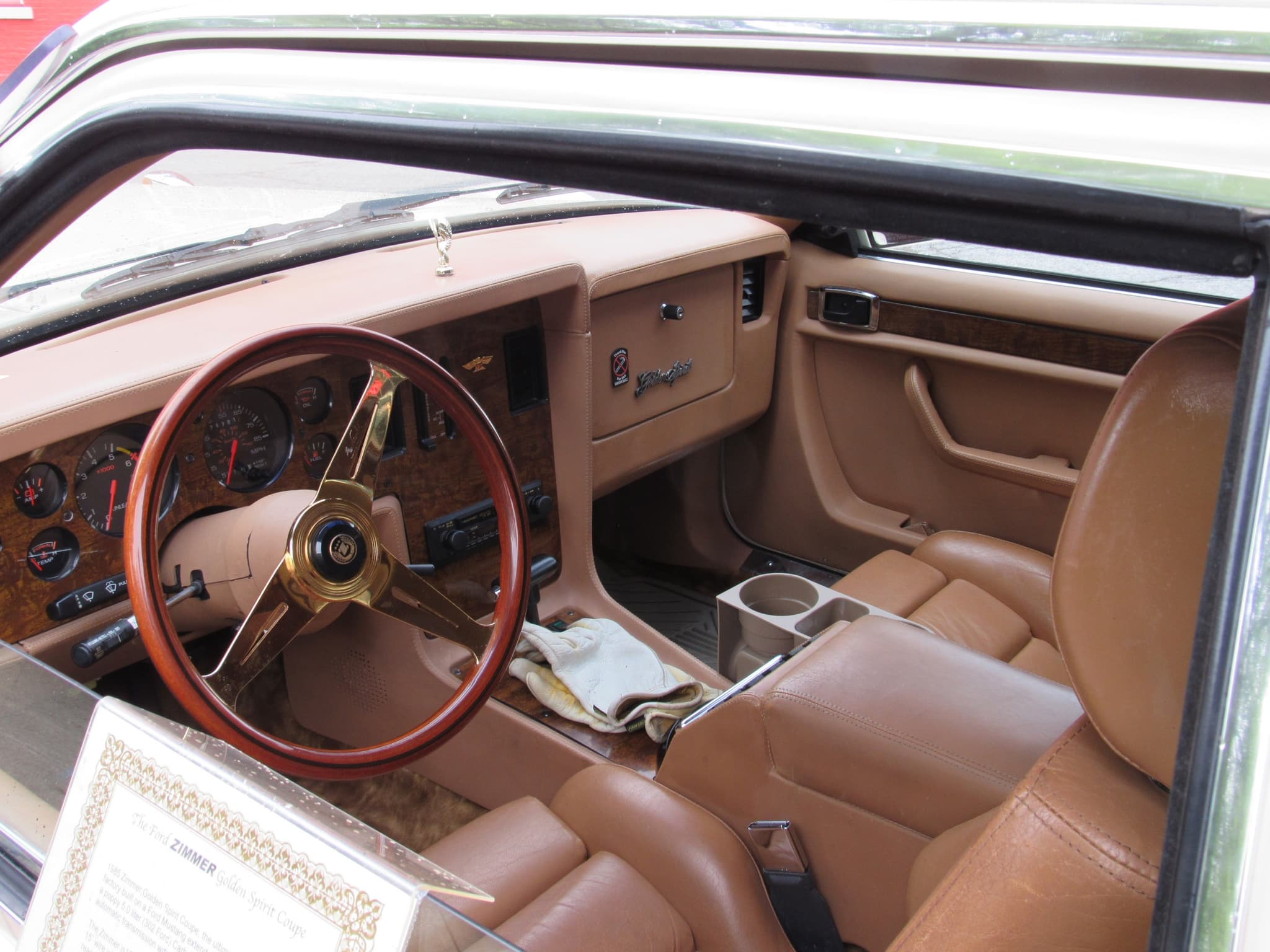 A Golden Spirit cockpit with a padded tan dashboard, a burr-walnut instrument panel, a gold-spoked wood-rim wheel and tan leather seats.
