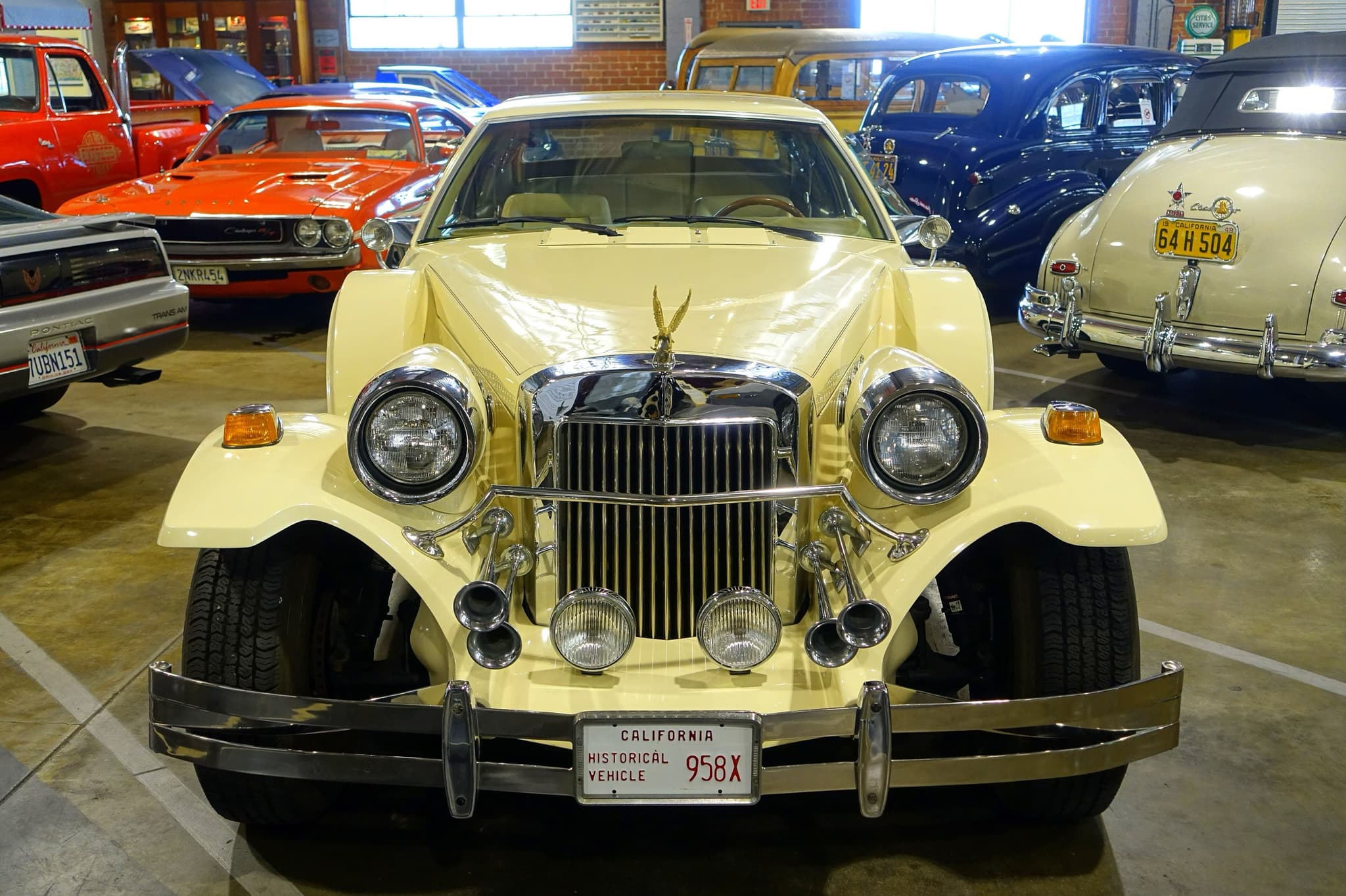 A yellow Golden Spirit seen head-on in a museum, its tall grille between two headlamps and two fog lamps and trumpet horns. Opens a larger view