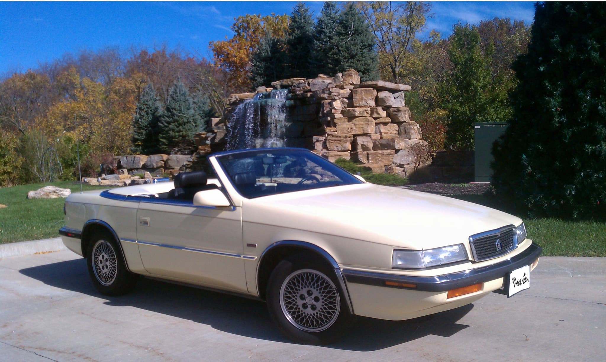 A cream Chrysler TC by Maserati convertible with its top down on a driveway.