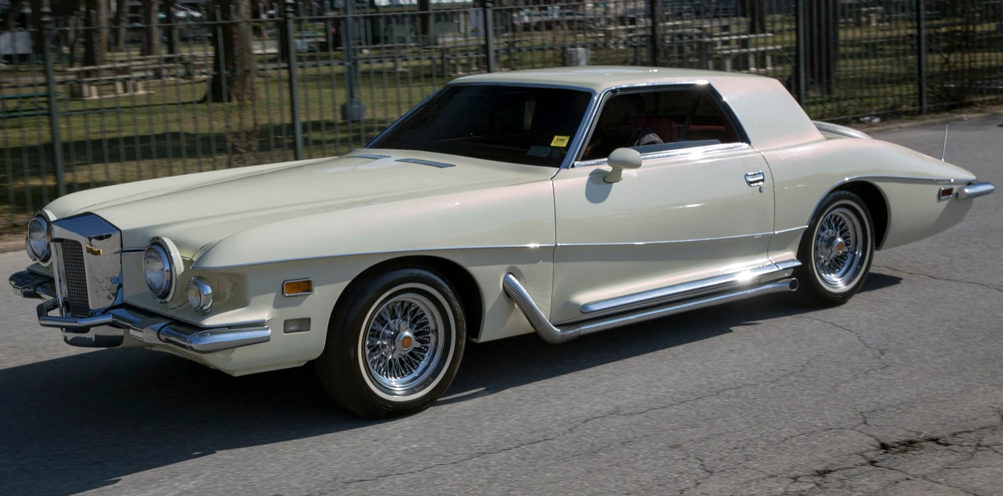 A white Stutz Blackhawk coupé with an upright chrome grille and wire wheels on a park road.