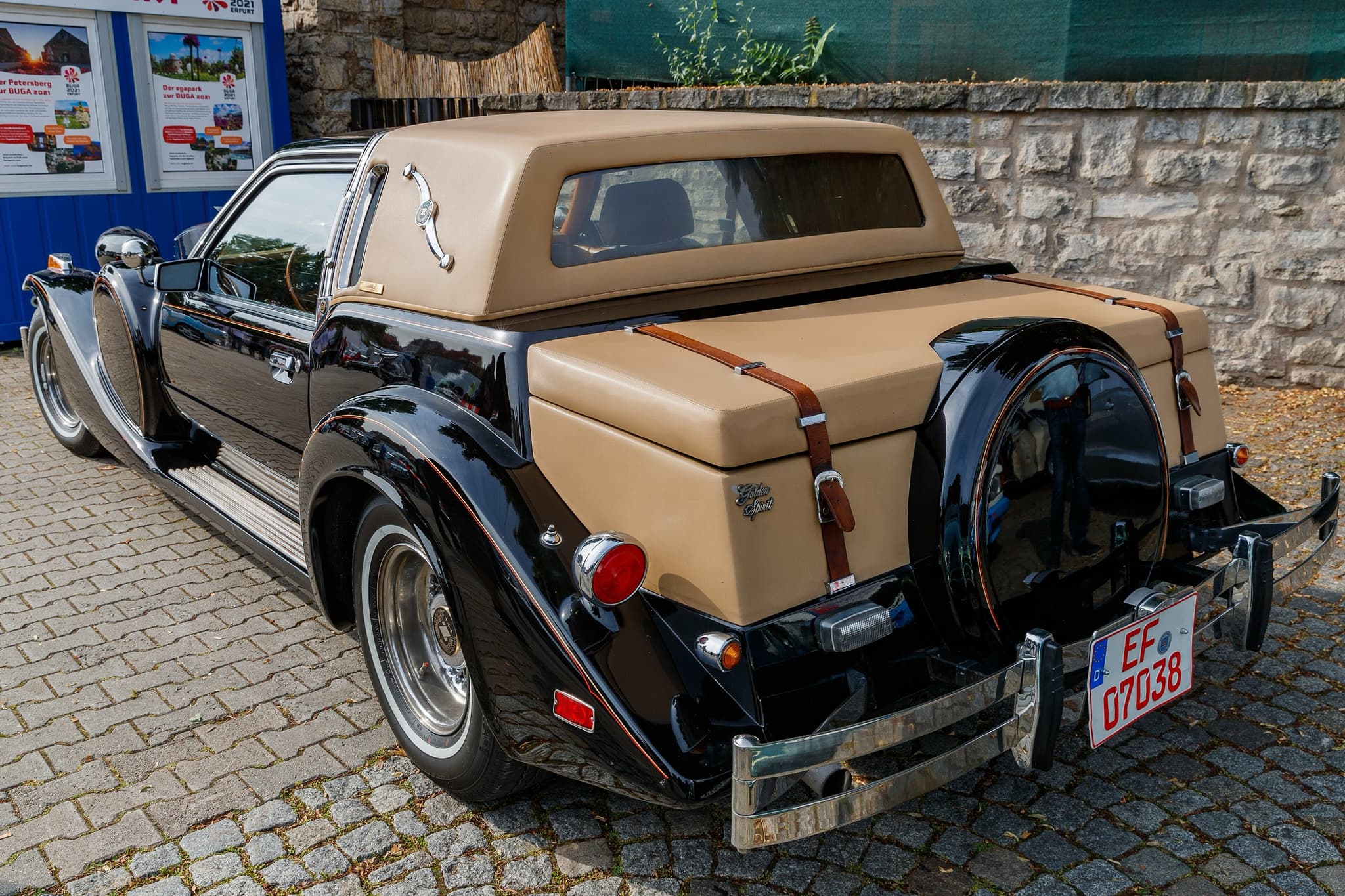 The rear of a black Golden Spirit with a tan padded roof, trunk straps and a black spare-wheel cover. Opens a larger view