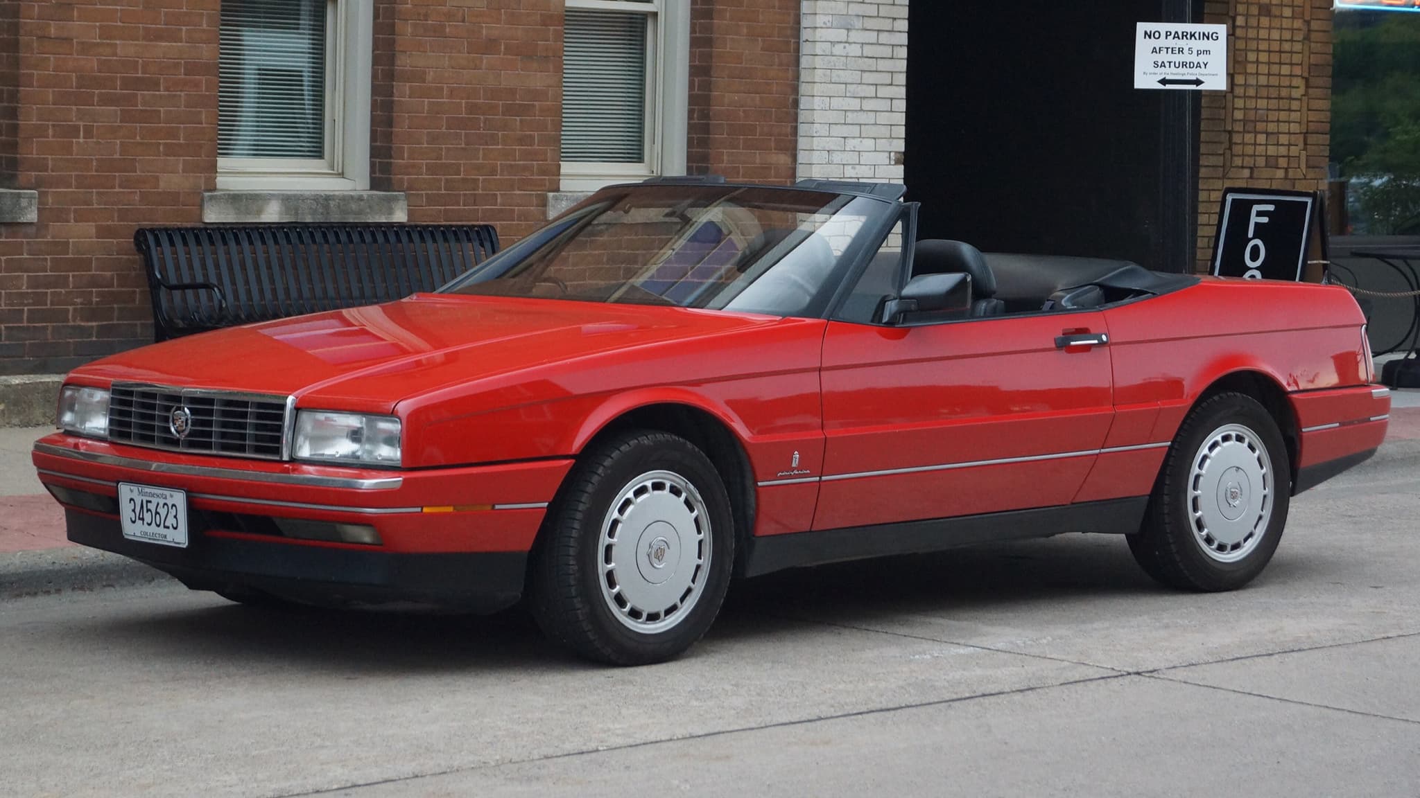 A red Cadillac Allanté convertible with its top down, parked on a town street.