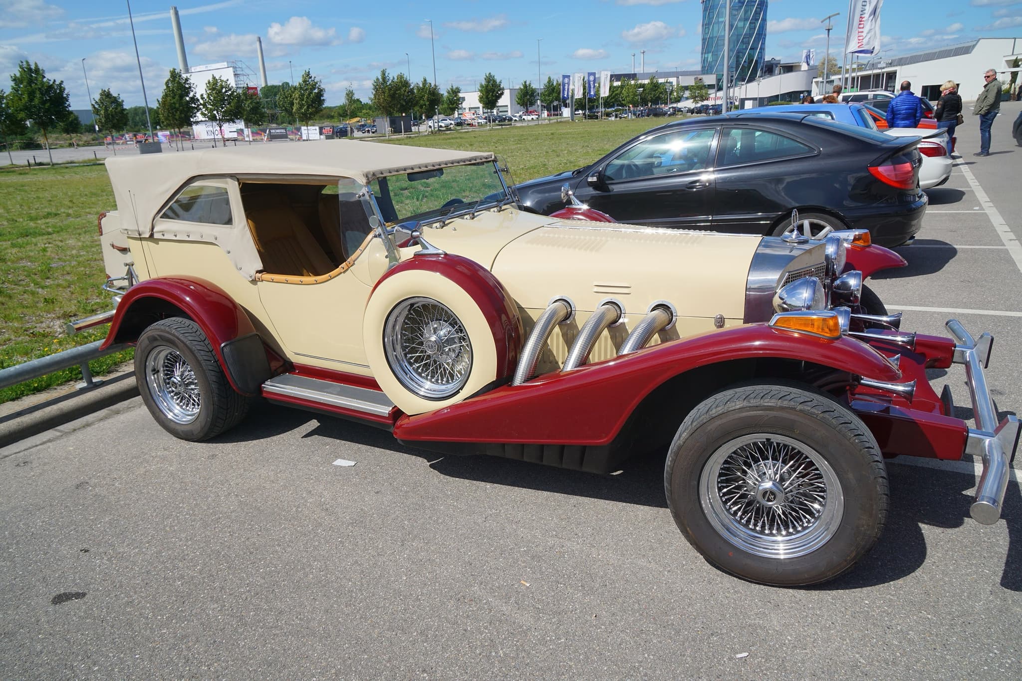 A cream and red Excalibur phaeton with its folding top up, chrome side exhausts and a side-mounted spare wheel.