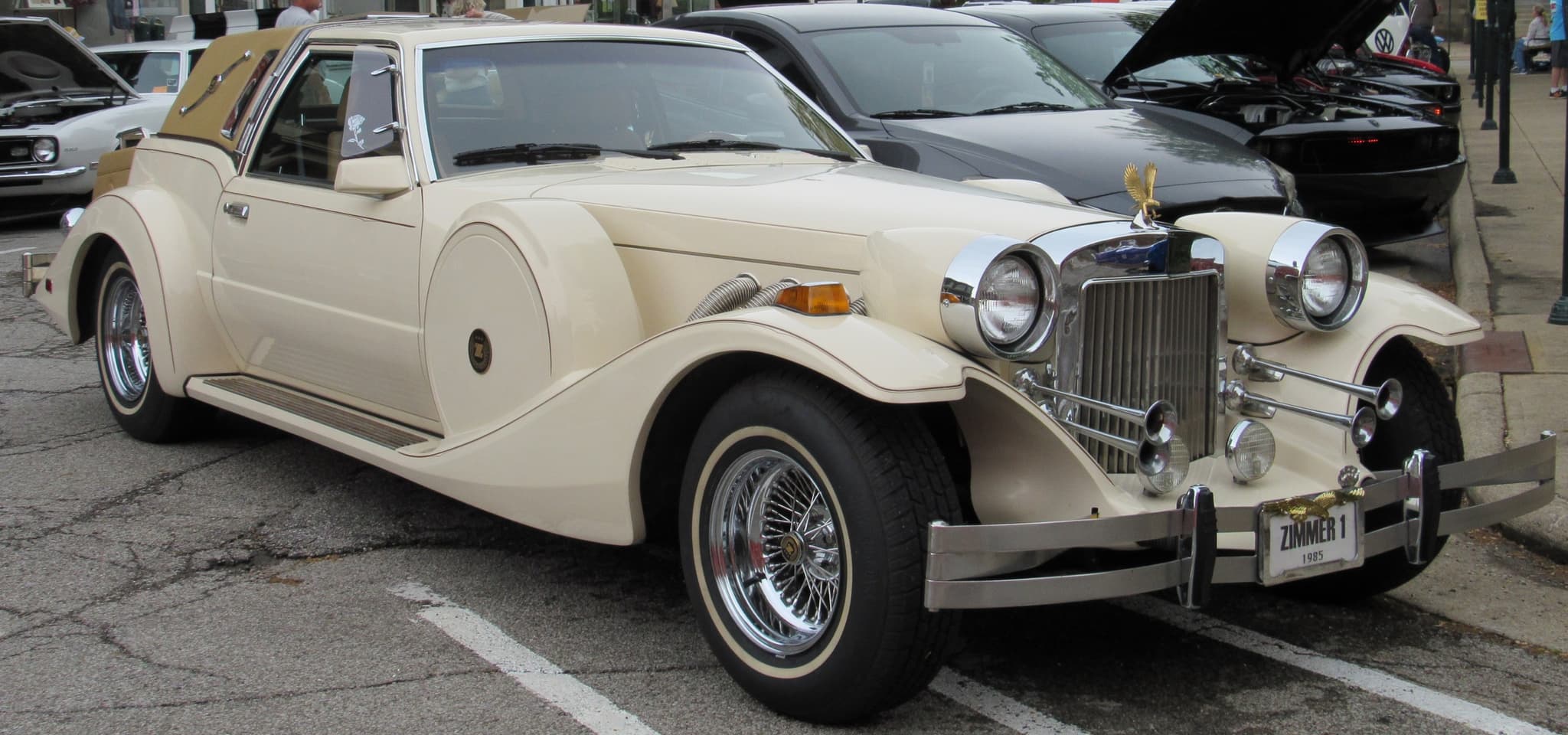 A cream Golden Spirit coupé with a gold eagle on its grille and a padded tan rear roof at an outdoor car show.