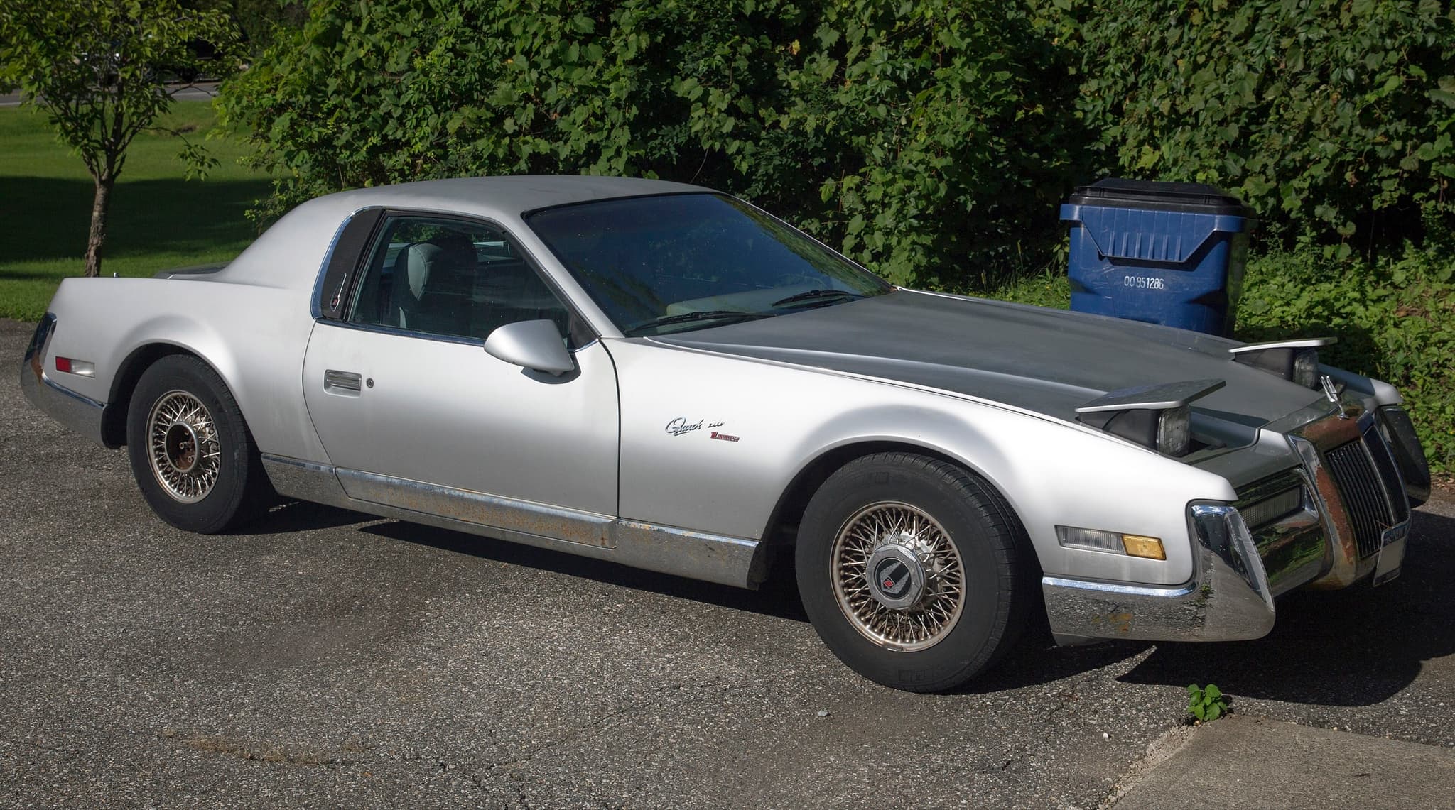 A silver QuickSilver with raised pop-up headlamps and a chrome front bumper, parked in a driveway.