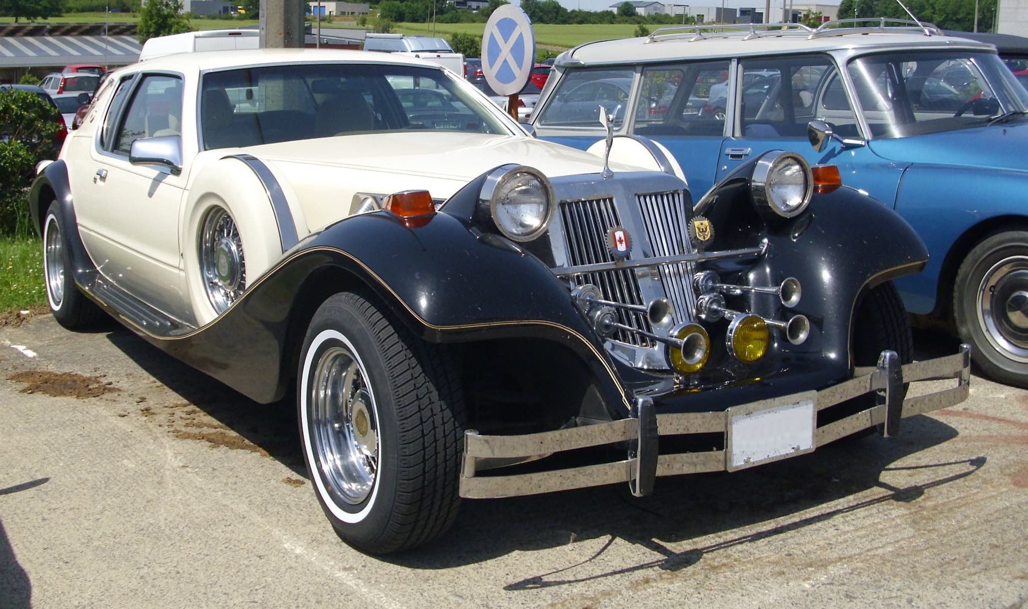 A cream and black Tiffany neoclassic car with a tall chrome grille, trumpet horns and yellow fog lamps.