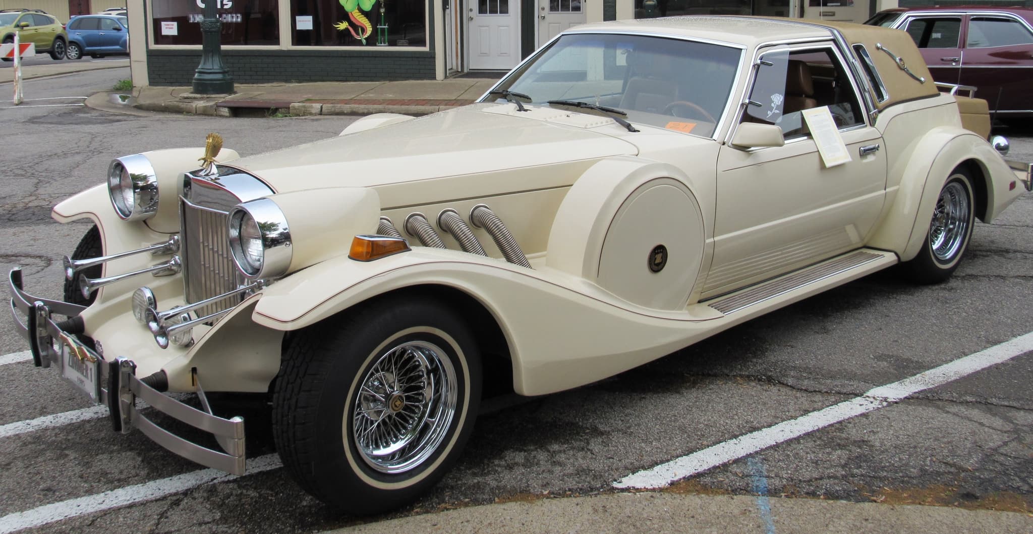 A cream Golden Spirit coupé with a tan padded rear roof, side exhausts and wire wheels, parked at a car show. Opens a larger view