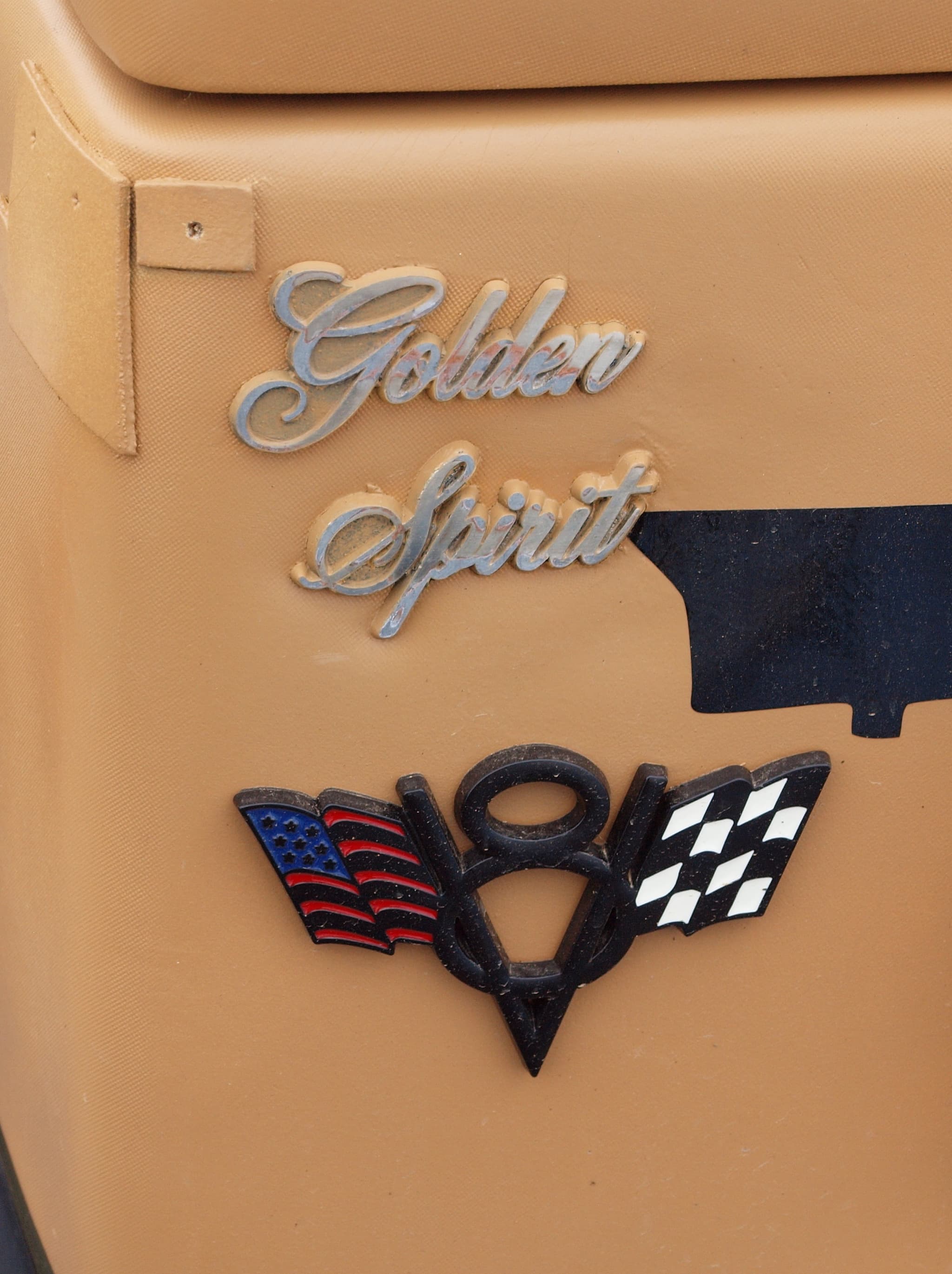The chrome words Golden Spirit on a tan padded panel above a large crossed-flags V8 badge.